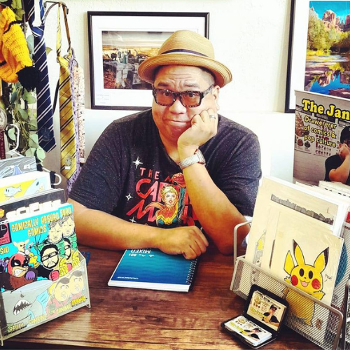 image of author Janimal sitting at a table with comics on display